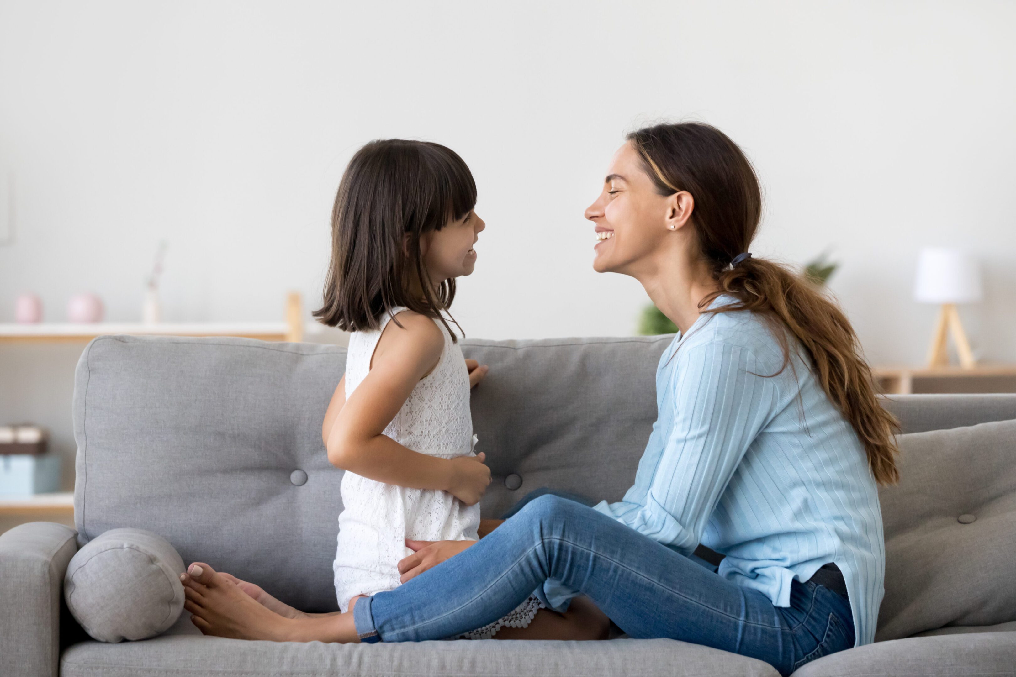 Mother spend time with little daughter talking sitting on couch Attractive woman and little girl sitting on comfortable couch at home. Young mother talking communicates with small adorable daughter. Best friends happy motherhood weekend together with kid concept