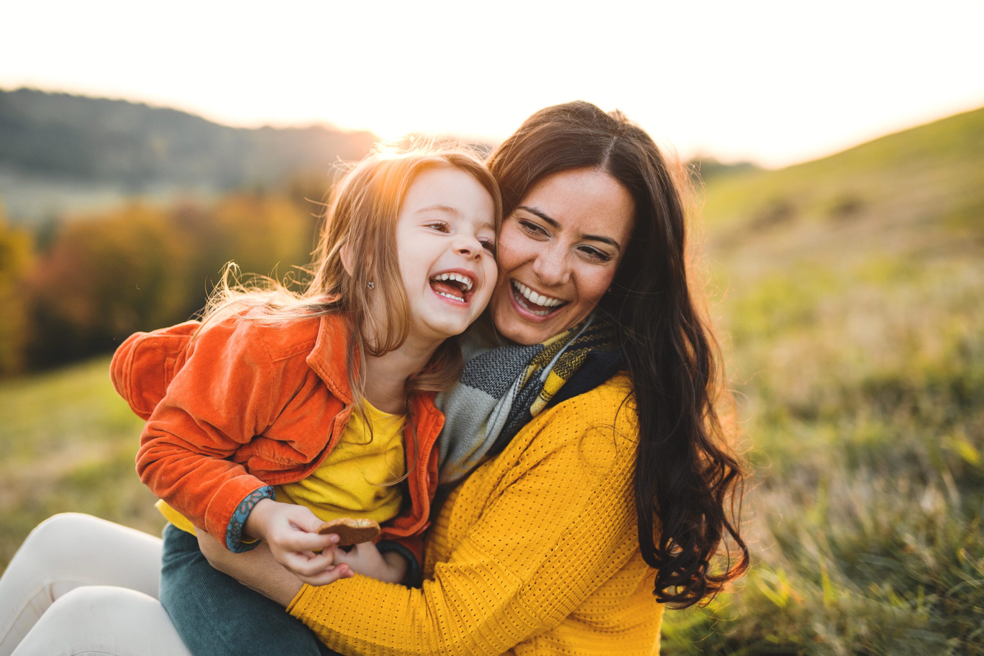 A portrait of young mother with a small daughter in autumn nature at sunset. A portrait of young mother with a small daughter sitting on a ground in autumn nature at sunset.