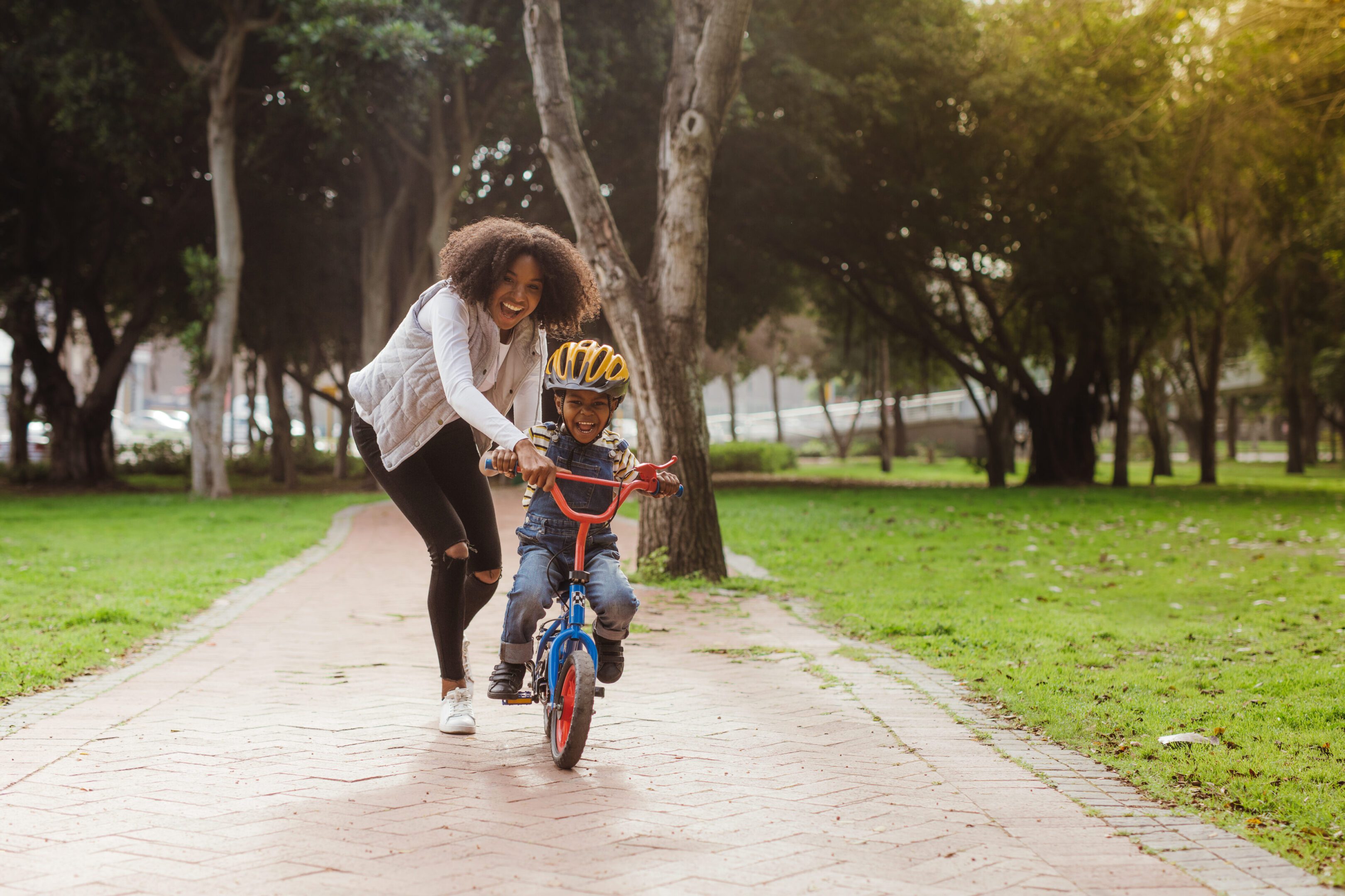 Mom teaching her son biking at park Cute boy learning to ride a bicycle with his mother. Woman teaching son to ride bicycle at park.